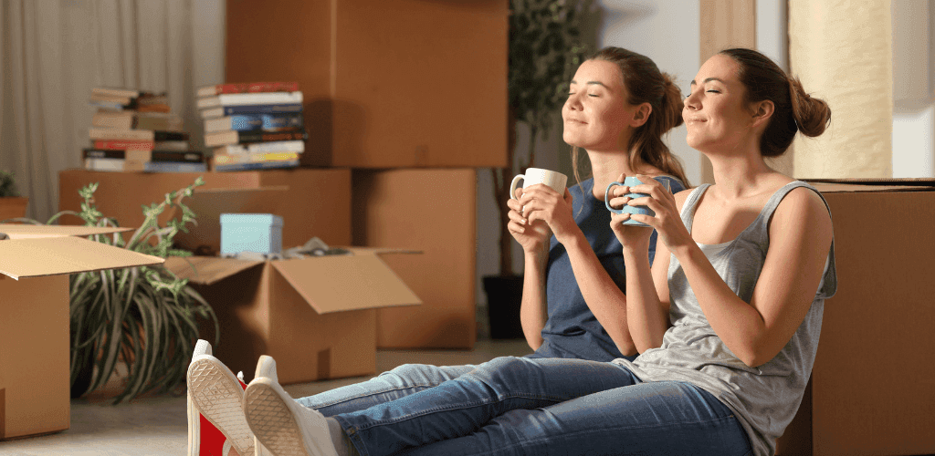 girls-sitting-beside-moving-boxes-drinking-coffee.png